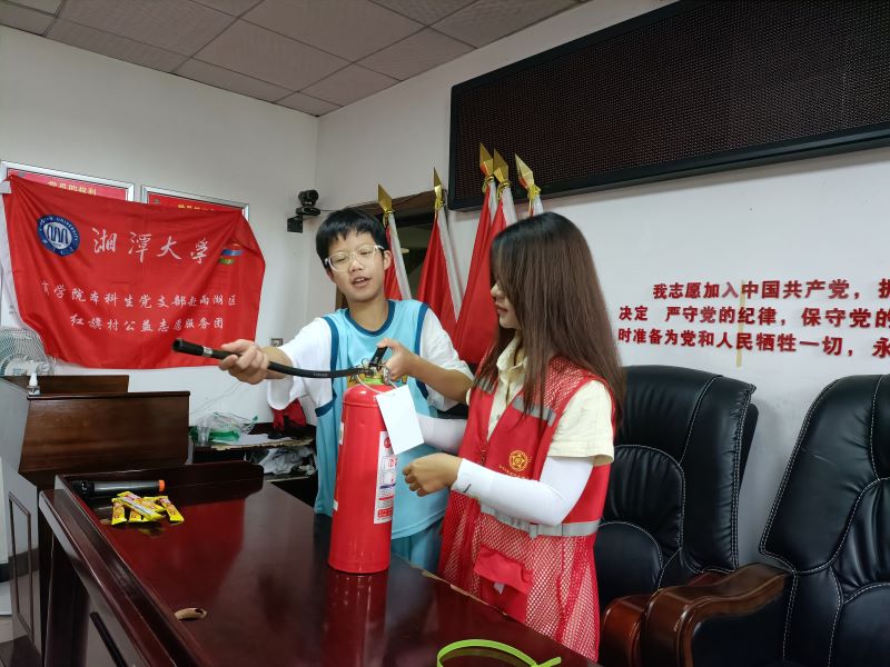 图为志愿者向小朋友演示如何使用灭火器的场景