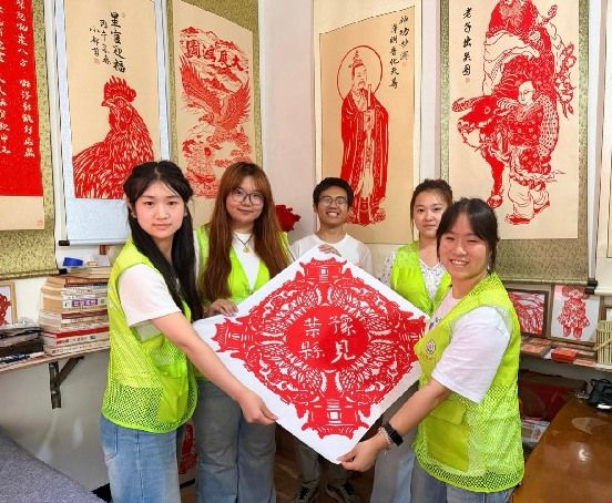图为实践队与剪纸非遗传承人都世奎共同展示刻有团队名称的剪纸作品。刘奕珂供图