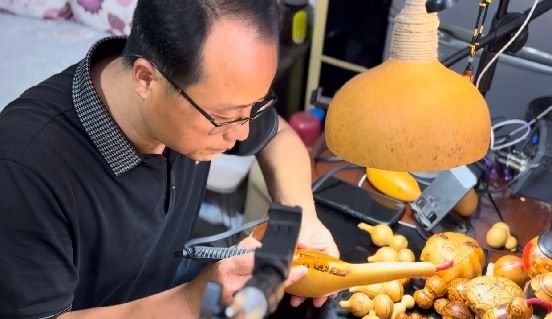图为葫芦烙画非遗传承人周军辉向实践队展示烙画制作过程。刘奕珂供图